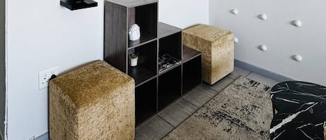 Una sala de estar moderna con un televisor de pantalla plana montado en la pared, un estante con adornos, un mueble de madera y dos otomanas cuadradas.