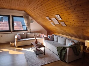 Un dormitorio estilo loft acogedor, con techo inclinado, un ventanal grande, un sofá, una mesita de centro y una lámpara.