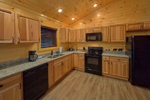 A kitchen with wooden cabinets, a microwave, a stove, and a refrigerator. - Hideaway Haven | Hot Tub, Game Room, Resort Pool, Fireplace + Free Attraction Tickets (Sevierville)