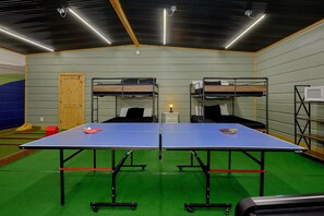 Een kamer met twee stapelbedden, een tafeltennistafel en een magnetron.