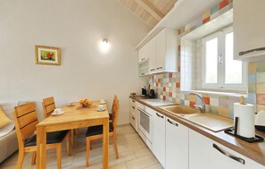 Eine kleine Küche mit Esstisch, Stühlen, Spüle und Fenster.
