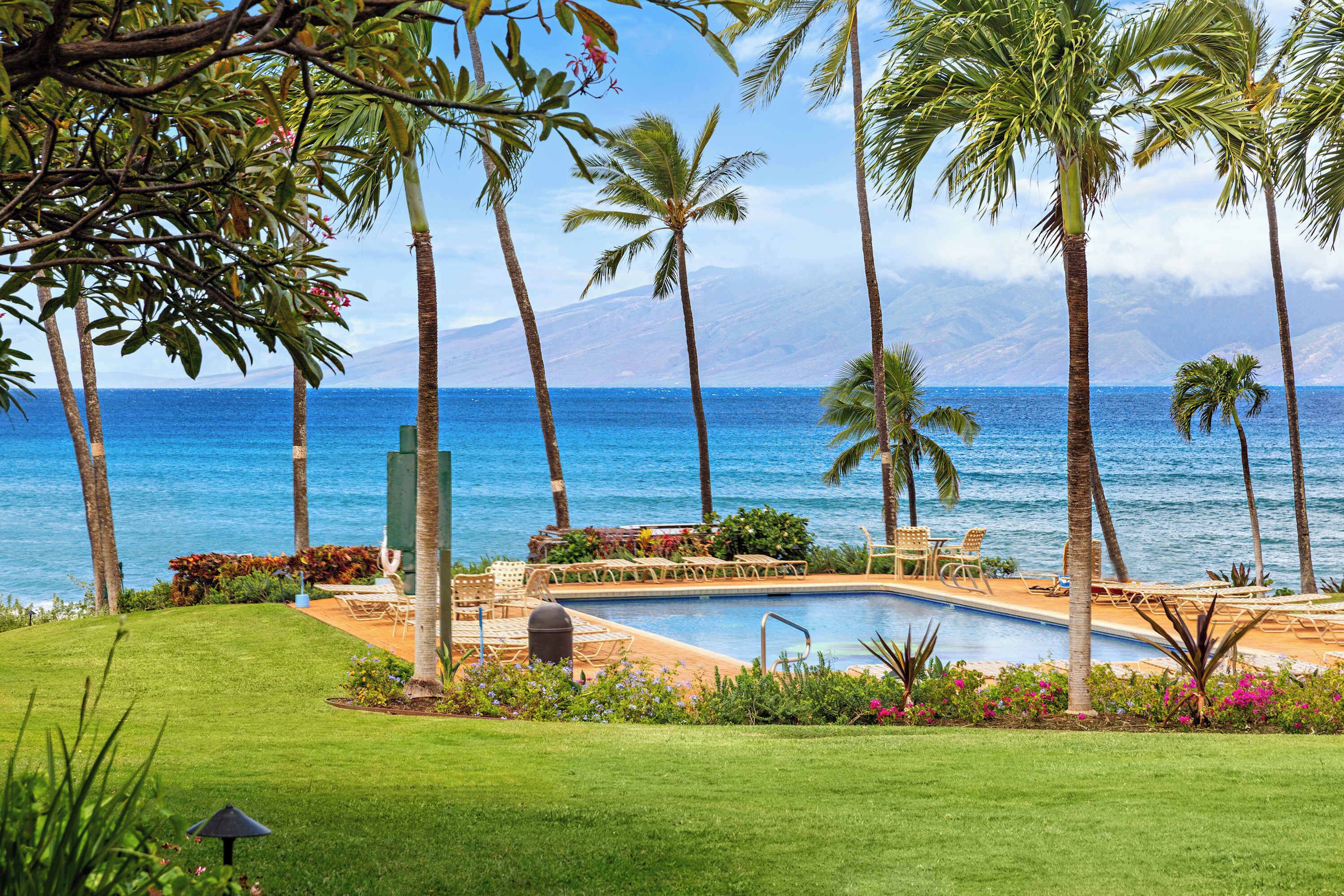 A pool area with lounge chairs and a view of the ocean.