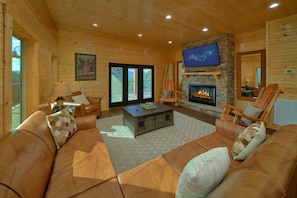A log cabin interior with a fireplace, leather sofas, a television, and a large window. - A Smoky Mountain Dream | Mountain Views | Private Pool | Hot Tub (Wears Valley)