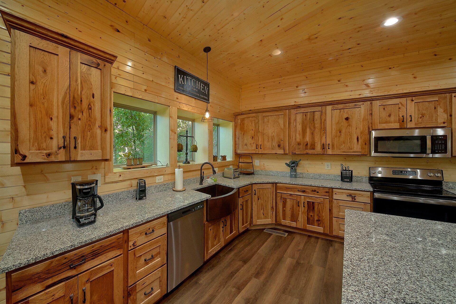 A kitchen with wooden cabinets, granite countertops, stainless steel appliances, and a window with a view of greenery.