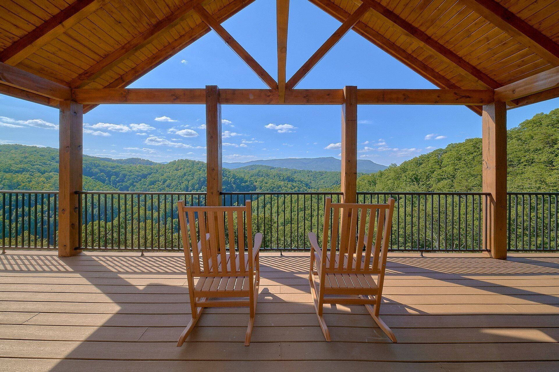 A wooden deck with two wooden chairs facing a scenic view of green hills and a clear sky.