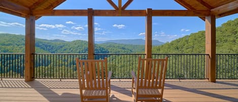 Eine Holzterrasse mit zwei Holzstühlen, die einen malerischen Blick auf grüne Hügel und einen klaren Himmel bietet.