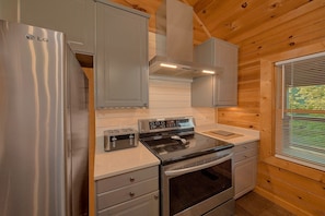 A compact kitchen with a stainless steel refrigerator, a built-in oven, a stove, and a toaster. - Douglas Dream | Smoky Mtn Views, Hot Tub, Lakefront, Game Room, Fireplace + Free Attraction Tickets (Sevierville)