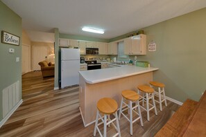 A compact kitchen with a central island, bar stools, and a dining area with a sofa. - Mill Creek Cottage | Hot Tub, Pigeon Forge, Fireplace + Free Attraction Tickets (Pigeon Forge)