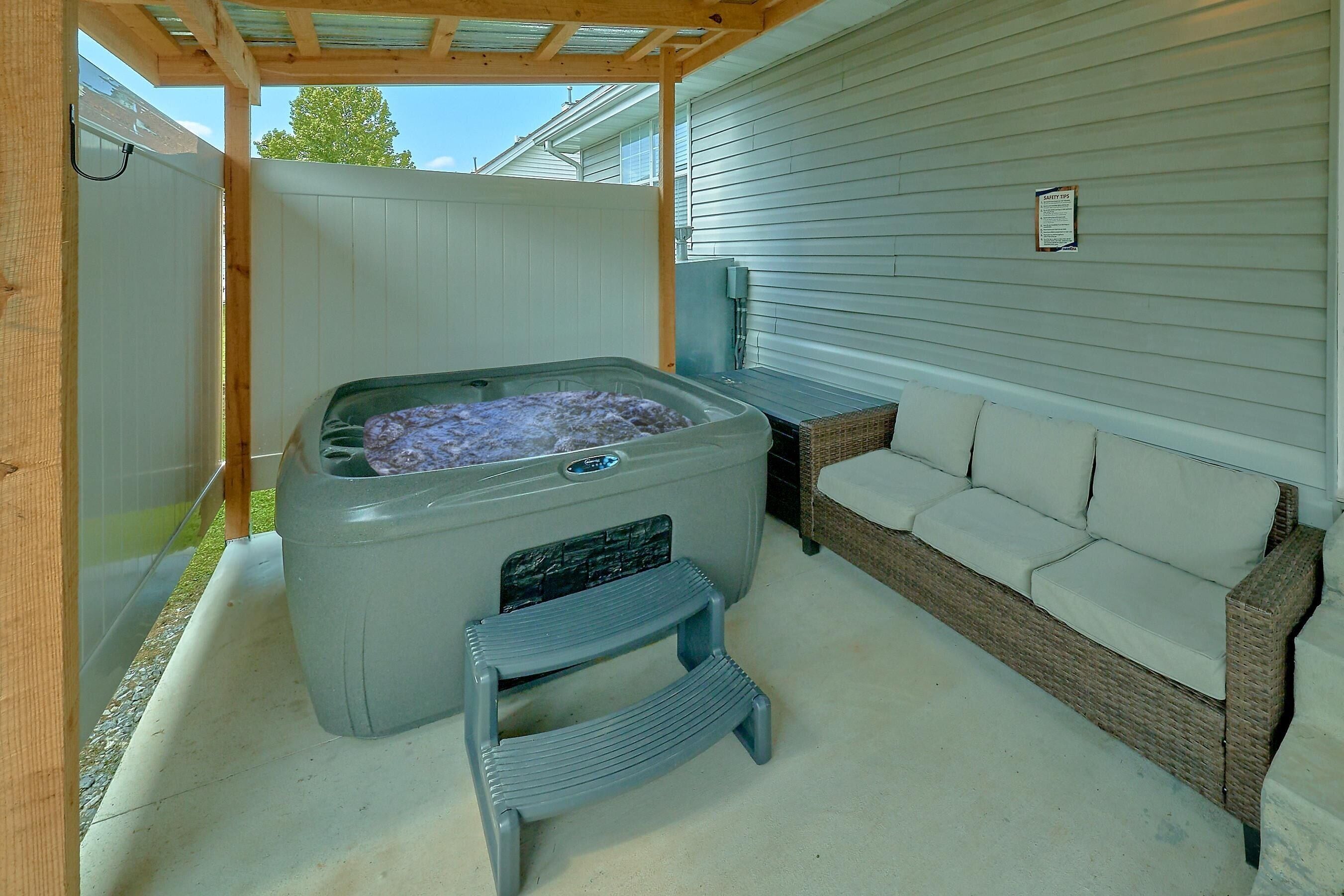 A hot tub with a step stool, a wicker sofa, and a safety tips sign on a house exterior.