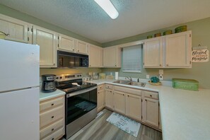 A kitchen with white cabinets, a microwave, stove, and a refrigerator. There is a window with blinds and a sign on the wall. - Mill Creek Cottage | Hot Tub, Pigeon Forge, Fireplace + Free Attraction Tickets (Pigeon Forge)