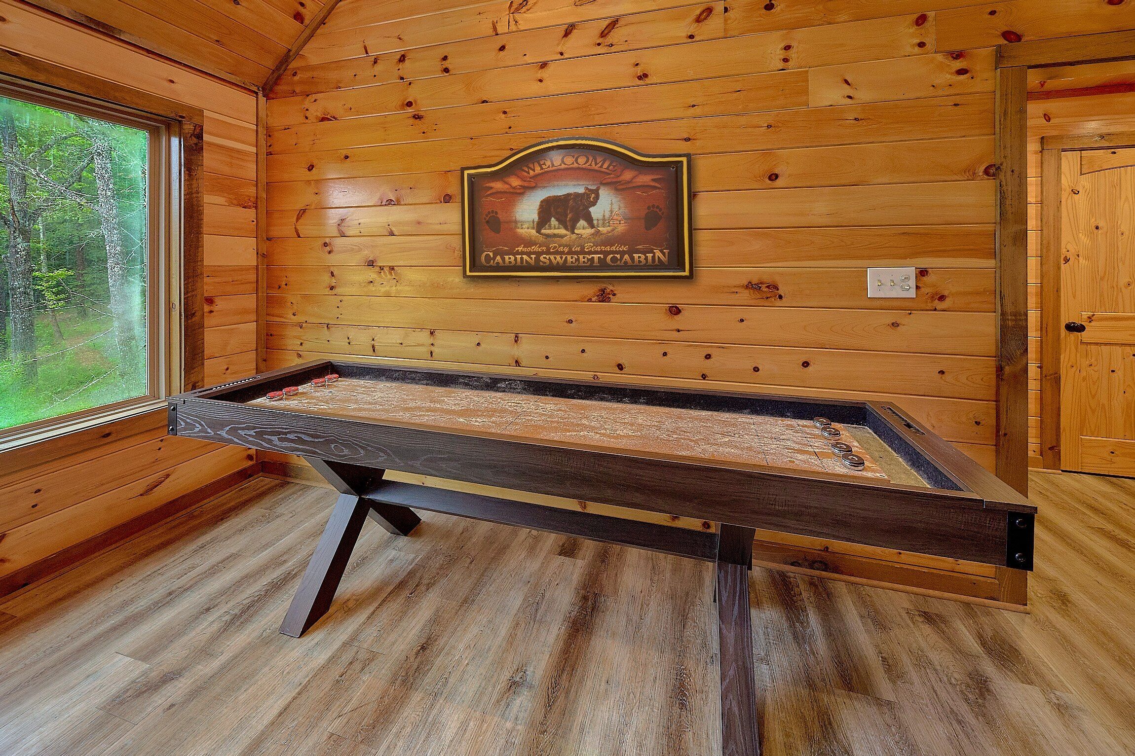 L’intérieur d’un chalet en bois, avec un plancher en bois, une table en métal sur laquelle est posé un jeu, et un panneau d’accueil accroché au mur.