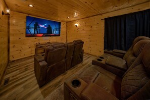 Ein Zimmer mit Holzwänden, Ledersesseln, einem Wand-Fernseher und einem dunklen Vorhang.