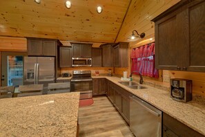 A kitchen with granite countertops, stainless steel appliances, wooden cabinets, and a red curtain. - Makin Waves | Private Pool, Theater, Hot Tub, Game Room, Sleeps 10 + Free Attraction Tickets (Wears Valley)