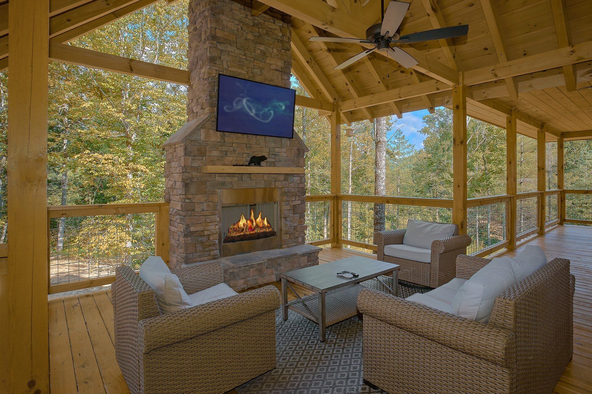 A covered outdoor seating area with wicker furniture, a stone fireplace, and a ceiling fan.