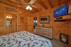 A wooden cabin interior with a bed, dresser, television, and a ceiling fan. - Chocolate Moose | Mountain Views | Hot Tub | Pool Table (Sevierville)