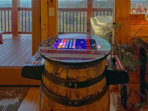 A wooden barrel with a glass top, a wooden deck, and a view of a mountainous landscape through a window. - Chocolate Moose | Mountain Views | Hot Tub | Pool Table (Sevierville)