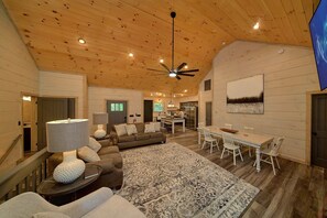 Ein geräumiges Wohnzimmer mit hoher Decke, Holzwänden, einem Essbereich und einer Küche.