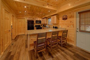 A wooden cabin interior with a kitchen, bar area, and a door. - Sunshine Vista | Hot Tub, Game Room, Fire Pit, Fireplace + Free Attraction Tickets (Sevierville)