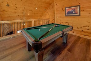A pool table with balls and cues in a room with wooden walls and a railing. - Sunshine Vista | Hot Tub, Game Room, Fire Pit, Fireplace + Free Attraction Tickets (Sevierville)