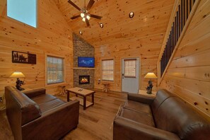 A log cabin interior with a fireplace, television, and wooden furniture. - Sunshine Vista | Hot Tub, Game Room, Fire Pit, Fireplace + Free Attraction Tickets (Sevierville)
