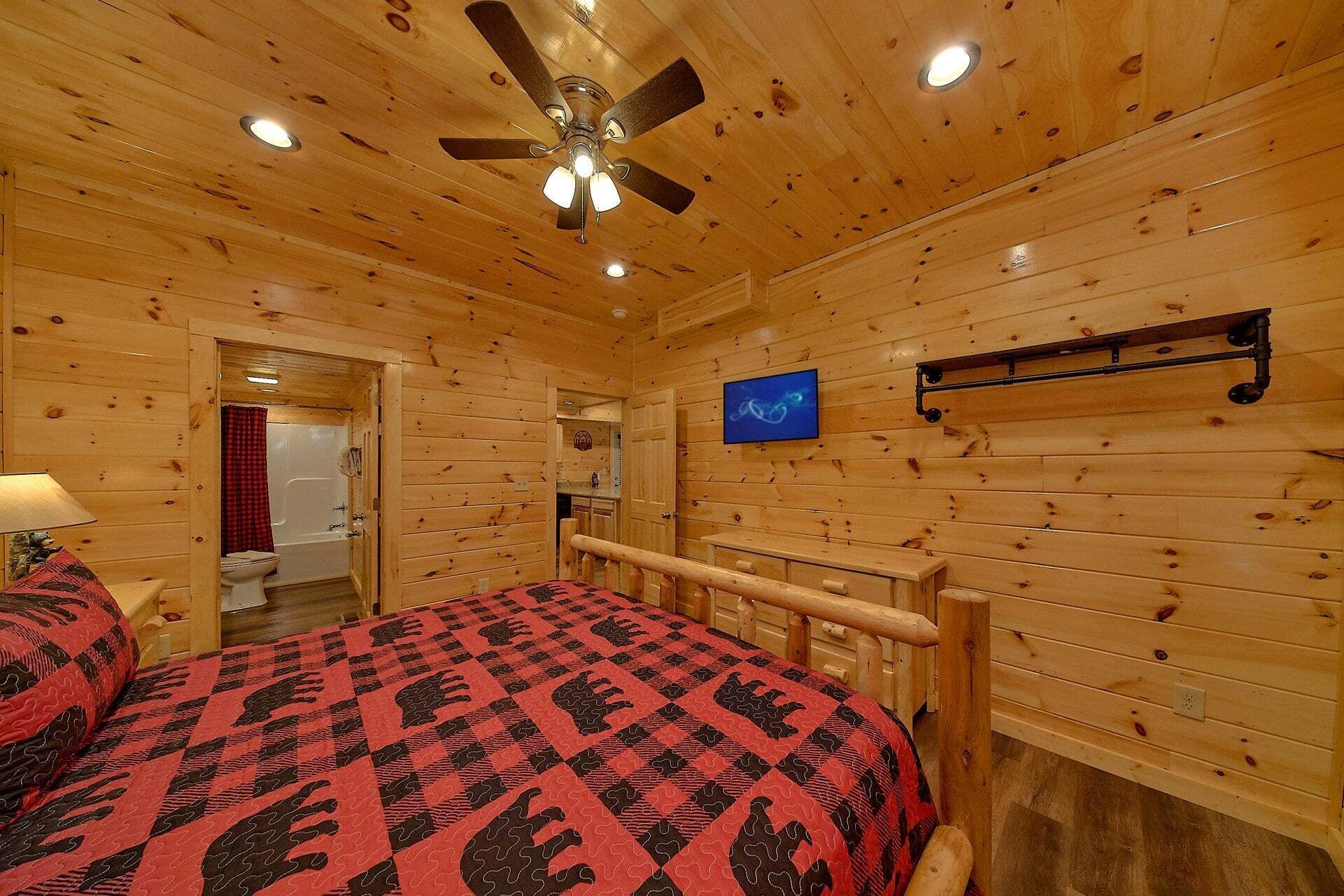 A wooden cabin bedroom with a bed, a ceiling fan, a mounted television, and a wooden railing.