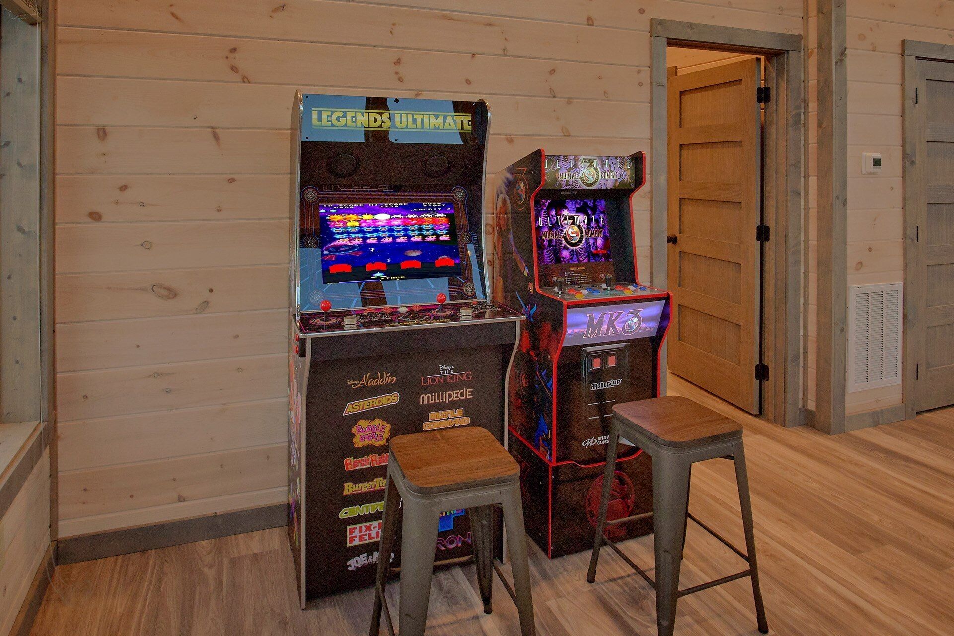 Arcade machines and stools in a room with wooden walls and floors.