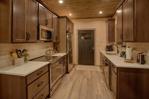 A kitchen with wooden cabinets, a microwave, a refrigerator, and a toaster. - Gatlinburg Splash | Private Pool, Mtn Views, Hot Tub, Game Room, Fireplace + Free Attraction Tickets (Gatlinburg)