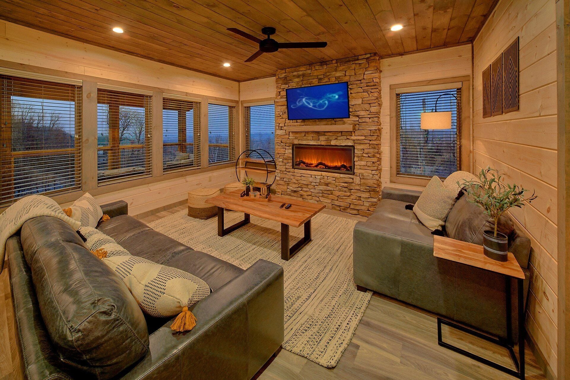 A cozy living room with a stone fireplace, leather sofas, a coffee table, and a flat-screen TV mounted above the fireplace.