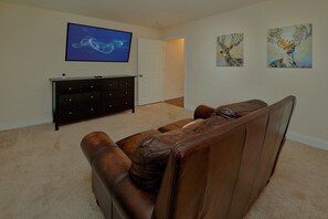 A living room with a brown leather sofa, a flat-screen TV mounted on the wall, a dark wooden cabinet, and two paintings on the wall. - Bear Necessities Vacation Home (Sevierville)