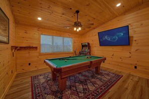 A pool table in a room with wooden walls and a ceiling fan.