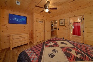 A wooden interior with a ceiling fan, a television, and a patterned rug.