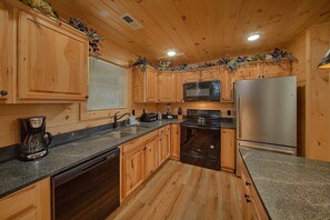 A kitchen with wooden cabinets, a stainless steel refrigerator, a dishwasher, and a granite countertop.