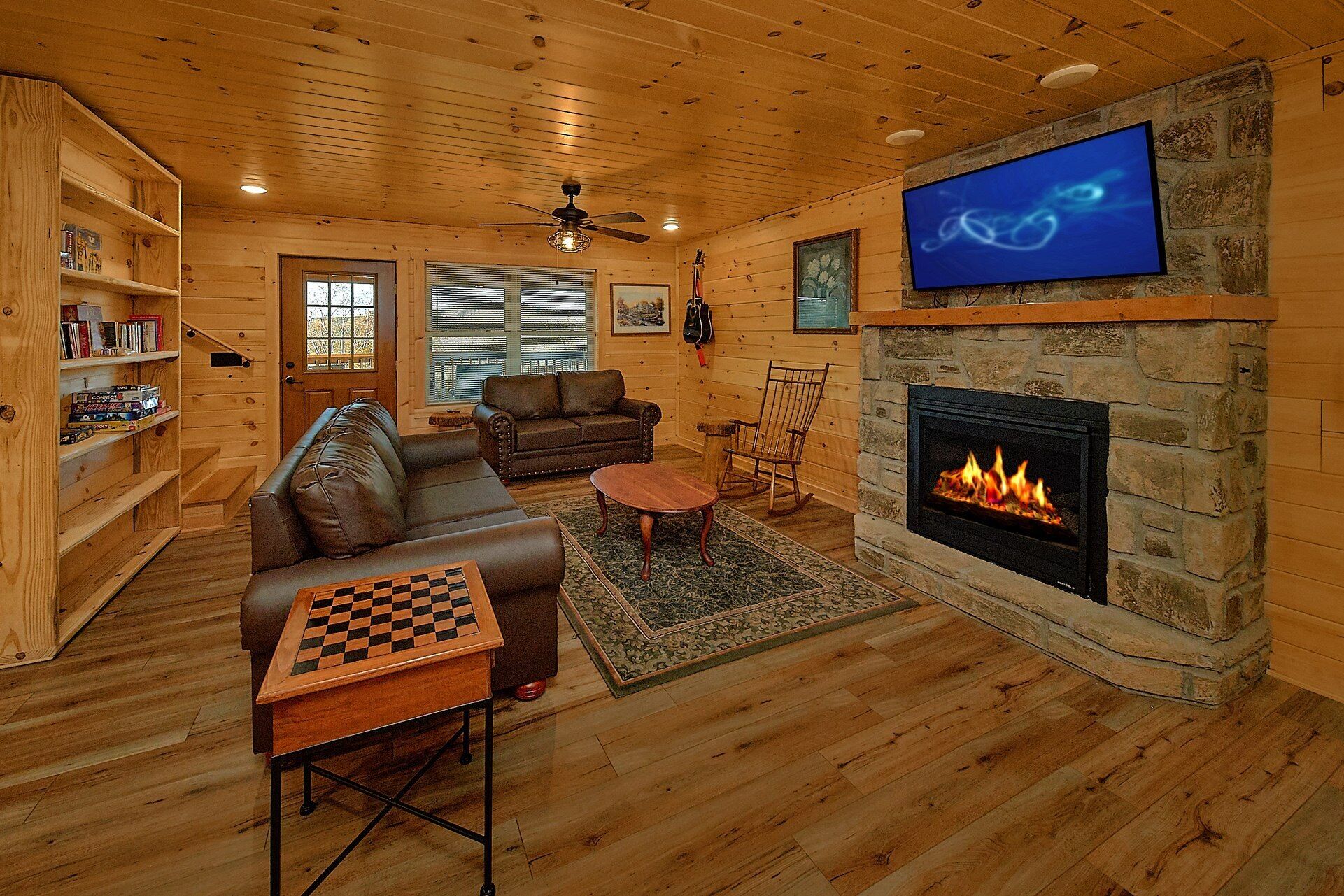 A cozy living room with a fireplace, a television mounted on the wall, and a chess table.
