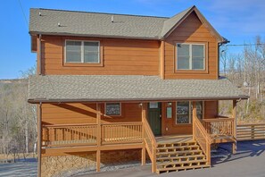 A two-story wooden house with a porch and a staircase leading to the entrance.