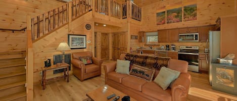 A cozy cabin interior with a wooden staircase, a living room with a sofa and a coffee table, and a kitchen area.