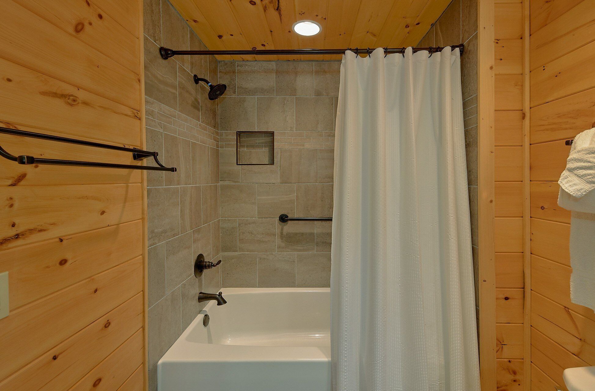 A wooden-paneled bathroom with a bathtub, shower, and a towel rack.