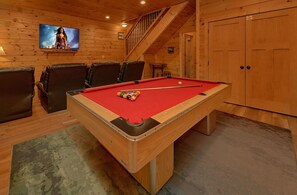 A pool table with a red felt surface, surrounded by leather chairs, in a room with wooden walls and a staircase. - Smoky Vista Lodge | Theater, Mtn Views, Hot Tub, Game Room, Sleeps 10 + Free Attraction Tickets (Gatlinburg)