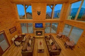 A wooden interior with a fireplace, seating area, and large windows. - Smoky Vista Lodge | Theater, Mtn Views, Hot Tub, Game Room, Sleeps 10 + Free Attraction Tickets (Gatlinburg)