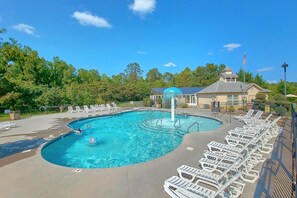A swimming pool with a water fountain, surrounded by lounge chairs and a building with a flag. - Mountain View 2504 | Mtn Views, Pigeon Forge, Resort Pool, Fireplace + Free Attraction Tickets (Pigeon Forge)