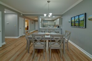 A dining area with a central table and chairs, a kitchen in the background, and a painting on the wall. - Mountain View 2504 | Mtn Views, Pigeon Forge, Resort Pool, Fireplace + Free Attraction Tickets (Pigeon Forge)