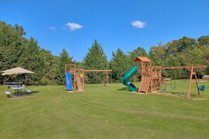 A playground with a slide and swings, surrounded by grass and trees. - Mountain View 2504 Condo Suite (Pigeon Forge)