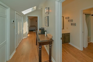 A hallway with a wooden floor, a table with a basket, a framed picture, and a light fixture. - Mountain Top Manor | Sleeps 18, Hot Tub, Game Room, King Suites, Fire Pit + Free Attraction Tickets (Sevierville)