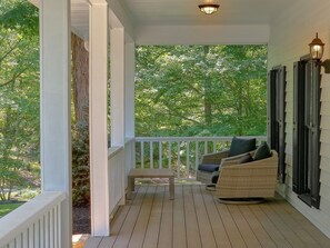 A covered porch with a bench and wicker furniture, surrounded by trees and a white railing. - Mountain Top Manor | Sleeps 18, Hot Tub, Game Room, King Suites, Fire Pit + Free Attraction Tickets (Sevierville)