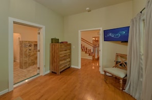 A hallway with a shower, wooden cabinet, staircase, and a television. - Mountain Top Manor | Sleeps 18, Hot Tub, Game Room, King Suites, Fire Pit + Free Attraction Tickets (Sevierville)