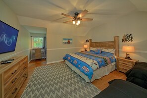 Ein Schlafzimmer mit Bett, Schreibtisch, Stuhl, Deckenventilator und Fernseher.