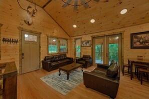 A log cabin interior with a wooden ceiling, a leather sofa, a coffee table, and a dining area. - Above Walden's Creek | Game Room | Hot Tub (Pigeon Forge)