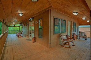 A wooden cabin with a porch, rocking chairs, and a view of the forest. - Above Walden's Creek | Game Room | Hot Tub (Pigeon Forge)