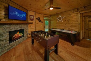 A room with a stone fireplace, a foosball table, and a pool table. - Above Walden's Creek | Game Room | Hot Tub (Pigeon Forge)
