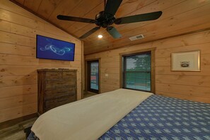 A wooden-paneled room with a bed, a ceiling fan, a television, and a framed picture on the wall. - A View From Above | Private Pool | Hot Tub | Mountain Views (Sevierville)
