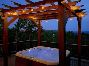 A hot tub under a wooden pergola with string lights, surrounded by a deck with a view of trees and hills. - A View From Above | Private Pool | Hot Tub | Mountain Views (Sevierville)